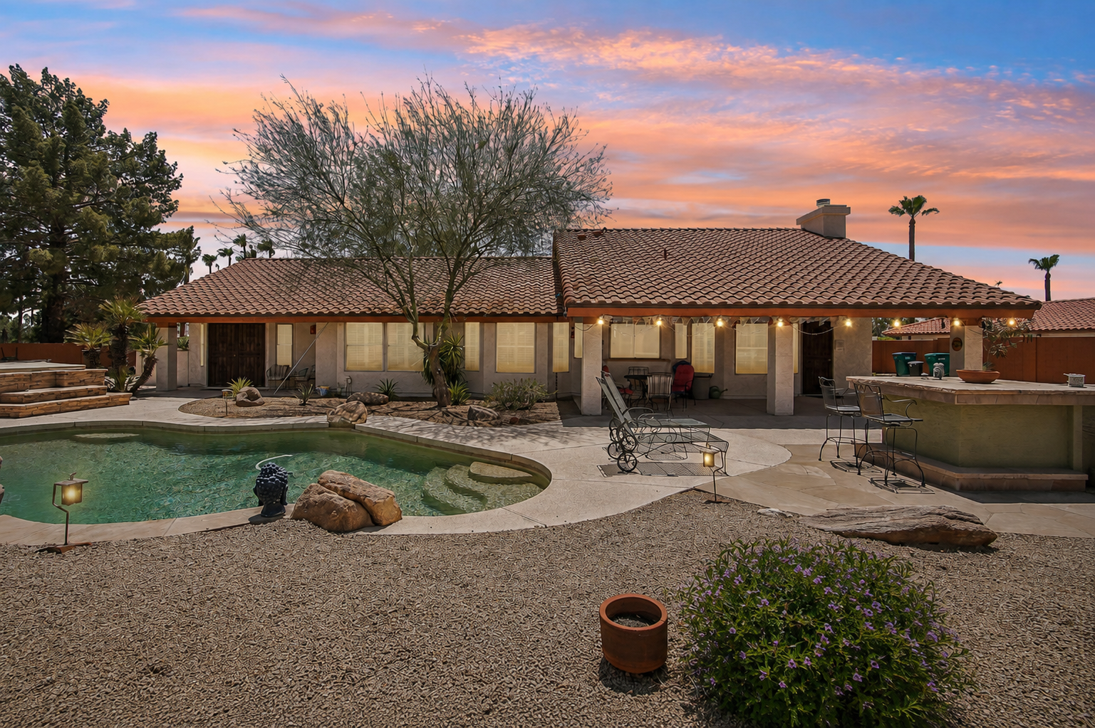 Backyard resort at dusk — pool, outdoor kitchen, and string lights under the covered patio