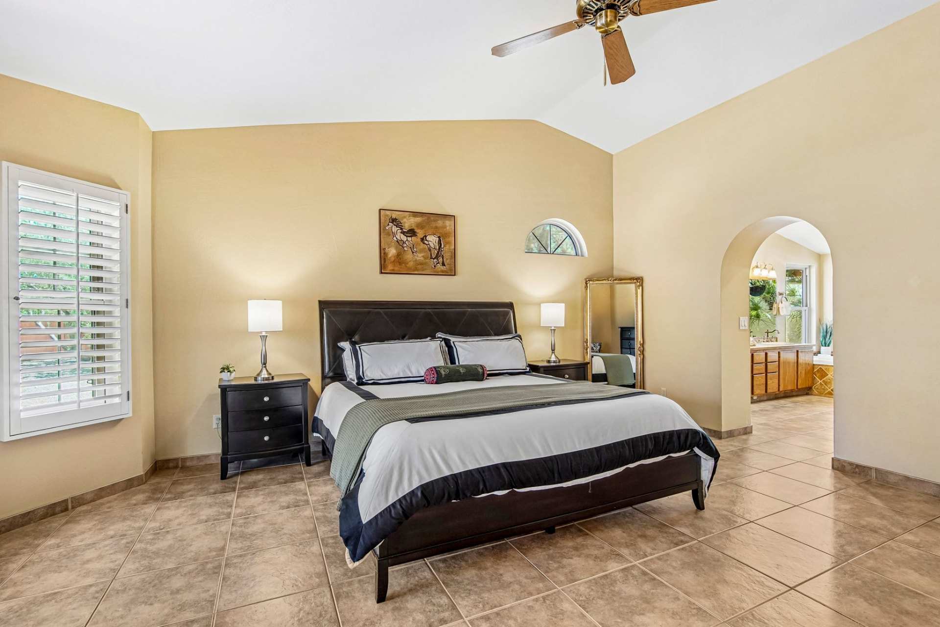Primary suite with vaulted ceiling, plantation shutters and tile floors